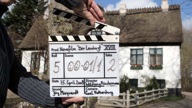 Filmklappe zu Dreharbeiten "Der Landarzt" vor Reetdachhaus (Quelle: M. Staudt / grafikfoto.de) Filmklappe zu Dreharbeiten "Der Landarzt" vor Reetdachhaus